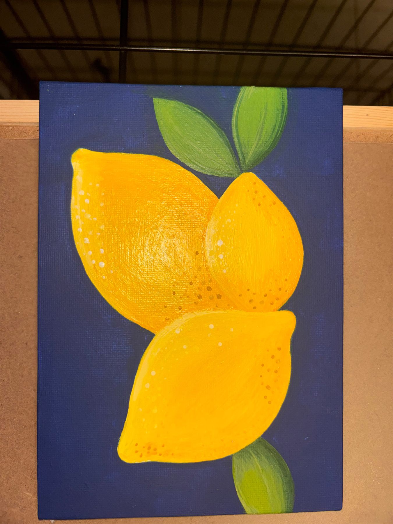 Acrylic painting of three bright yellow lemons with green leaves on a navy blue canvas