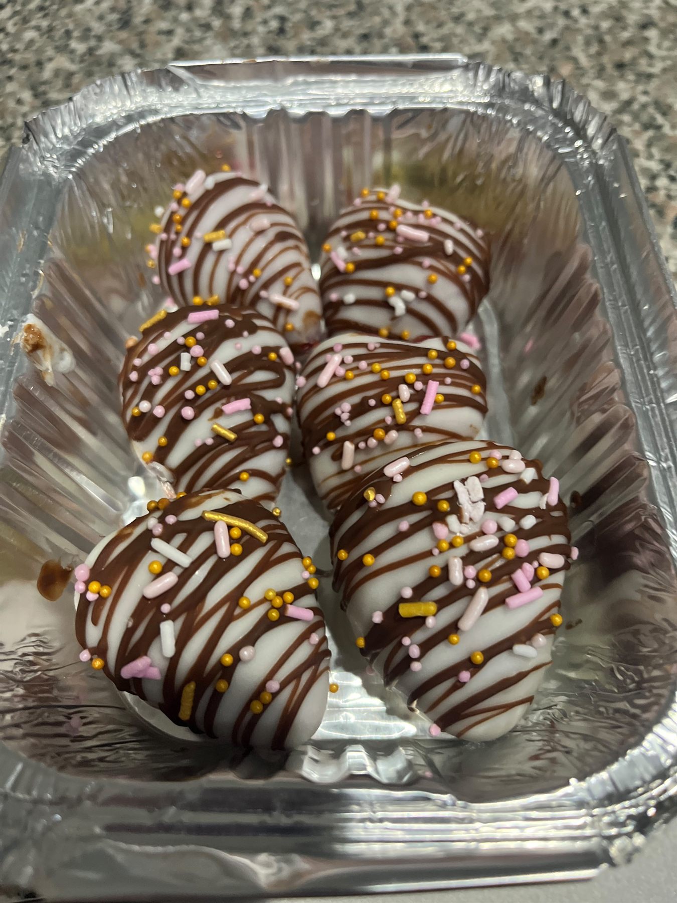 White chocolate covered treats drizzled with dark chocolate and topped with pink, gold and white sprinkles