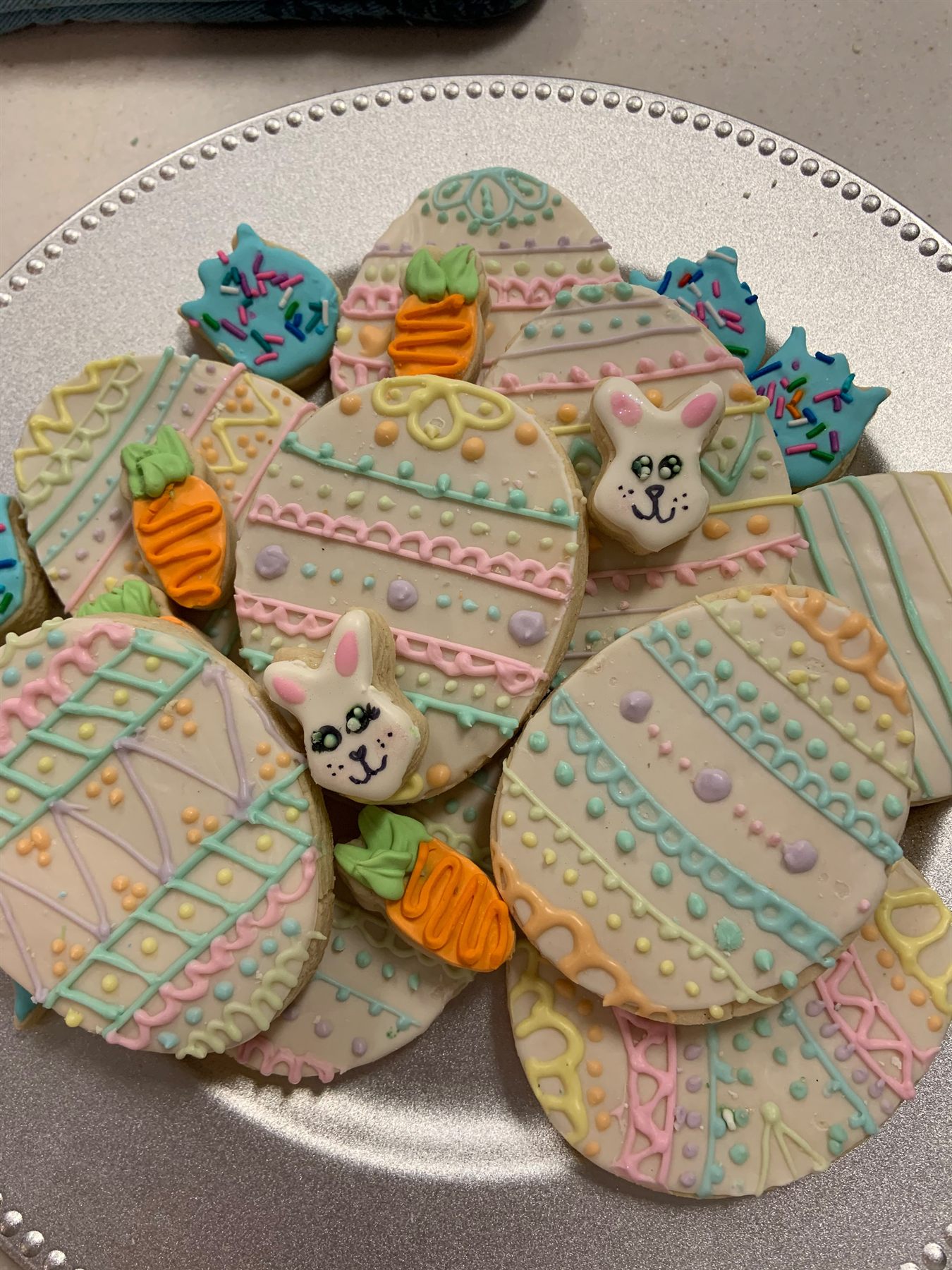 Plate of Easter cookies — large pastel-striped egg cookies with piped detail, plus bunny faces, carrots and sprinkle-topped chicks