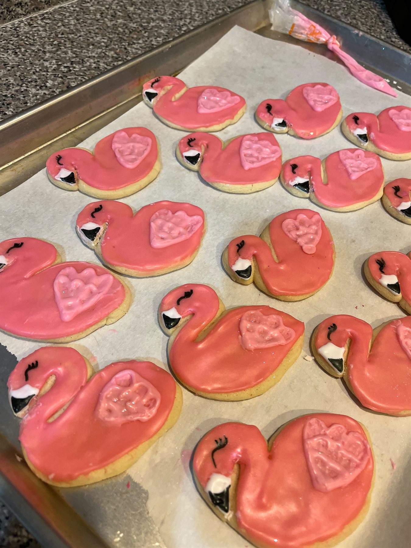 Tray of flamingo-shaped sugar cookies iced in coral pink with pale pink heart wings and black beaks