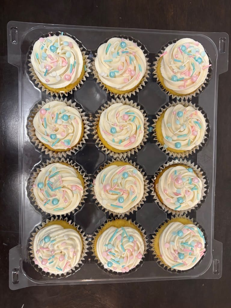 Clamshell box of vanilla cupcakes with swirled white buttercream and black and silver sprinkles, ready for a gender reveal