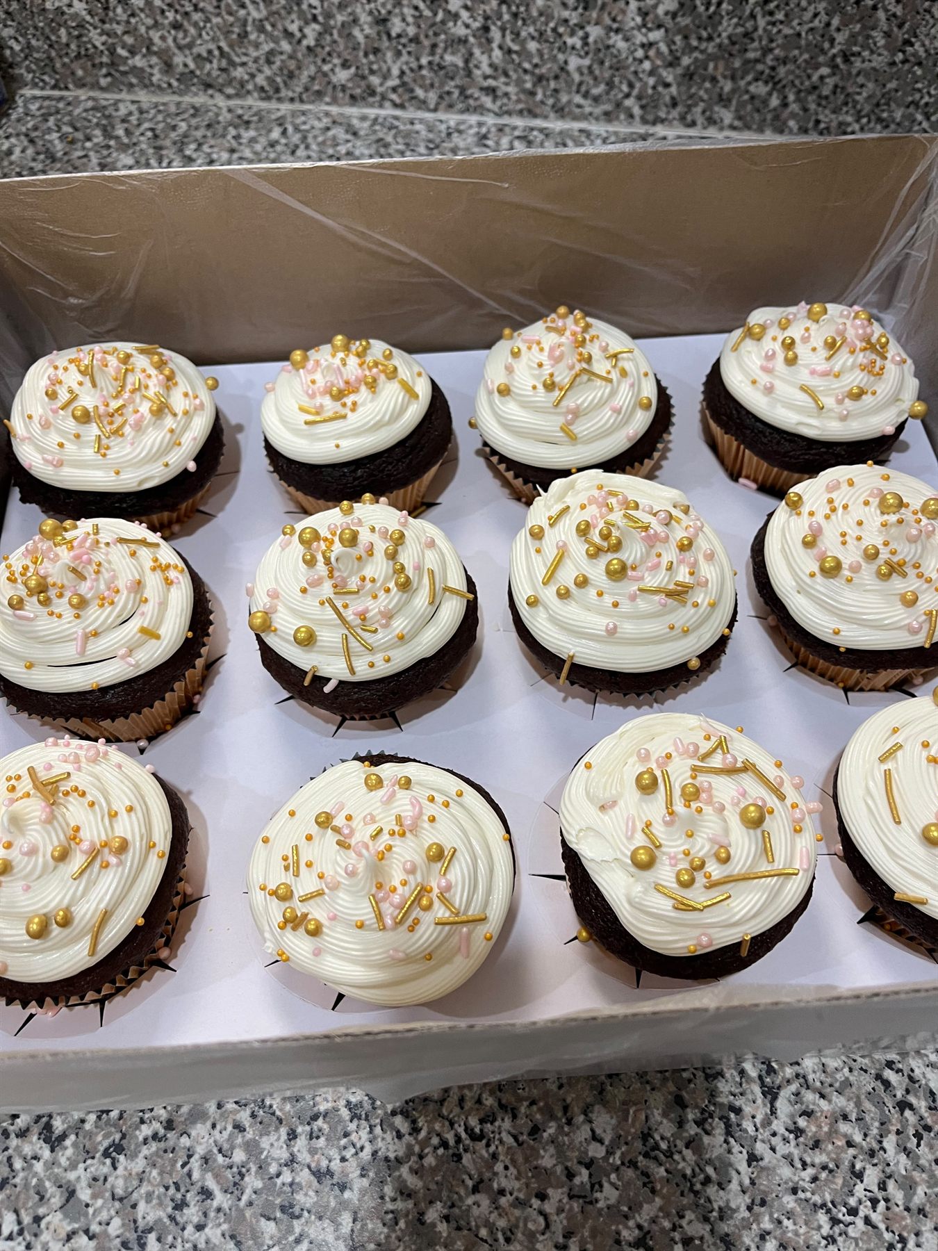 Box of chocolate cupcakes with swirled vanilla buttercream, gold pearls, gold sprinkles and pale pink beads