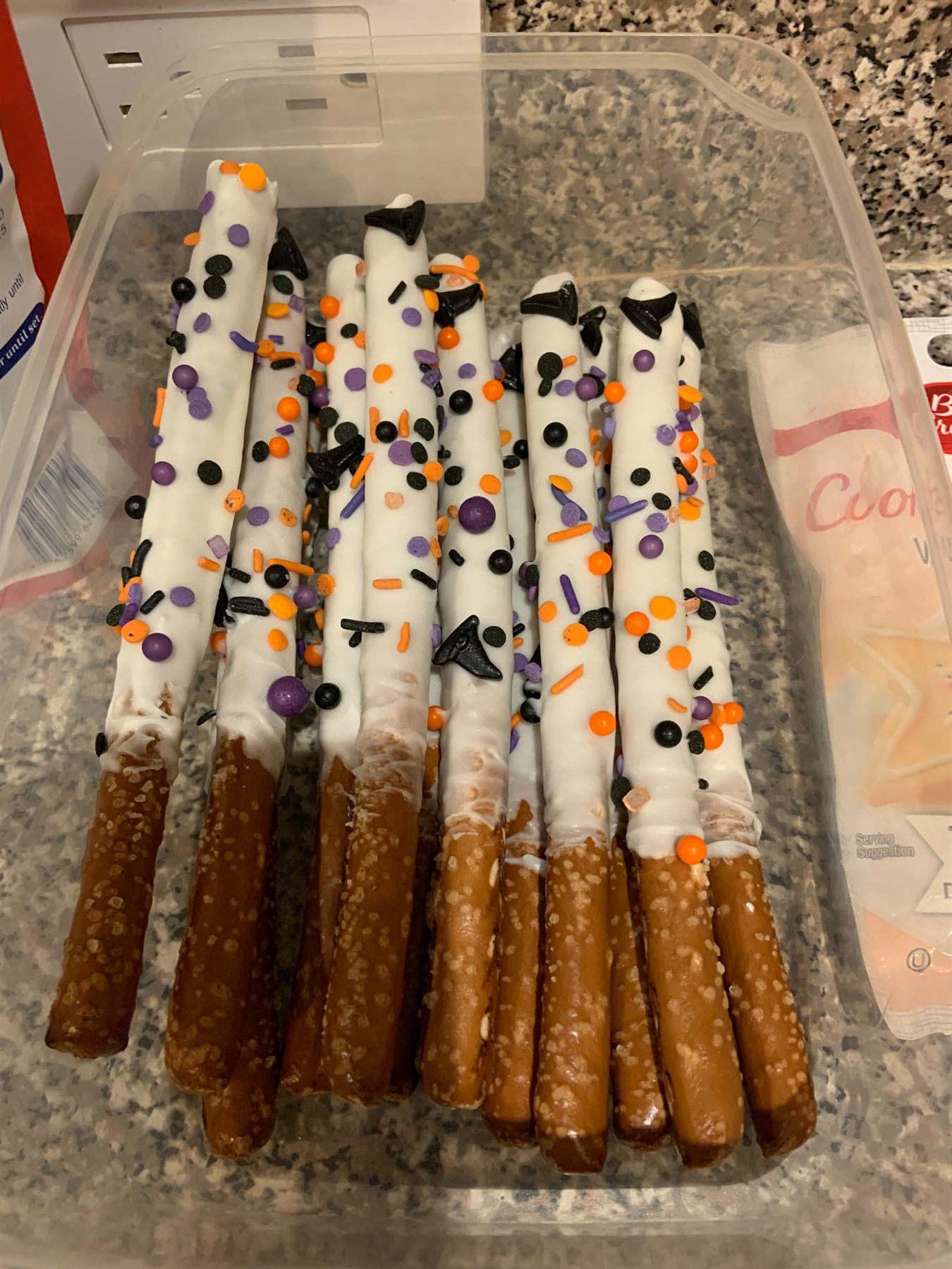 White chocolate dipped pretzel rods decorated with orange, purple and black Halloween sprinkles and candy bats