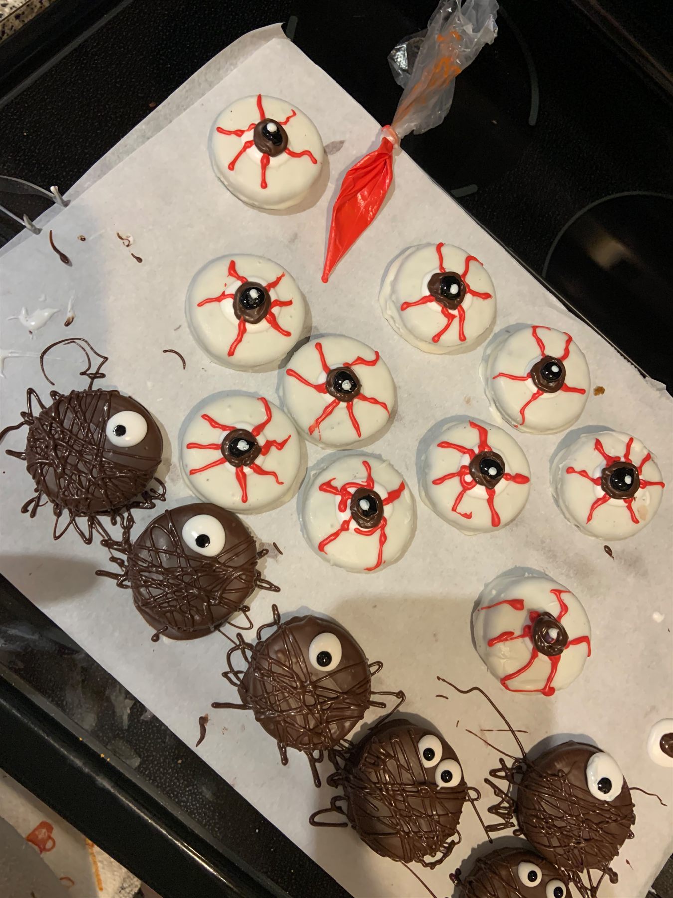 Halloween treats — white chocolate covered cookies piped as bloodshot eyeballs beside chocolate spiders with candy eyes