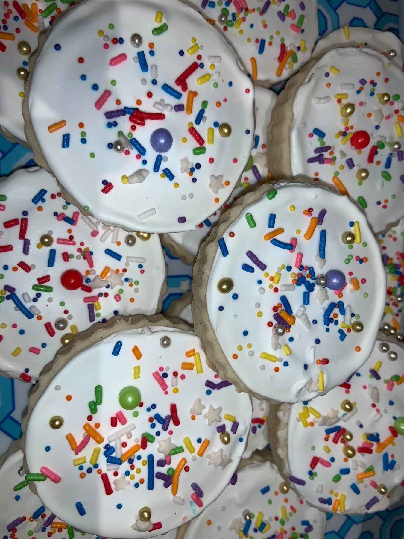 Close-up of round white-iced sugar cookies covered in rainbow sprinkles, gold and silver dragees and star confetti