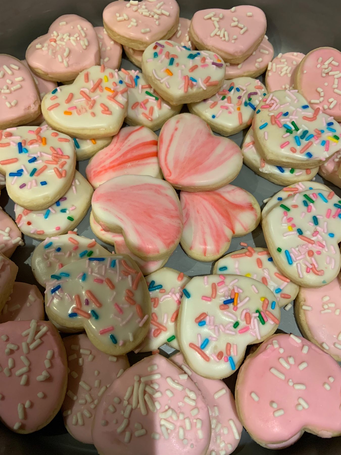 Heap of heart-shaped sugar cookies iced in pink and white with sprinkles, including marbled pink-and-white hearts